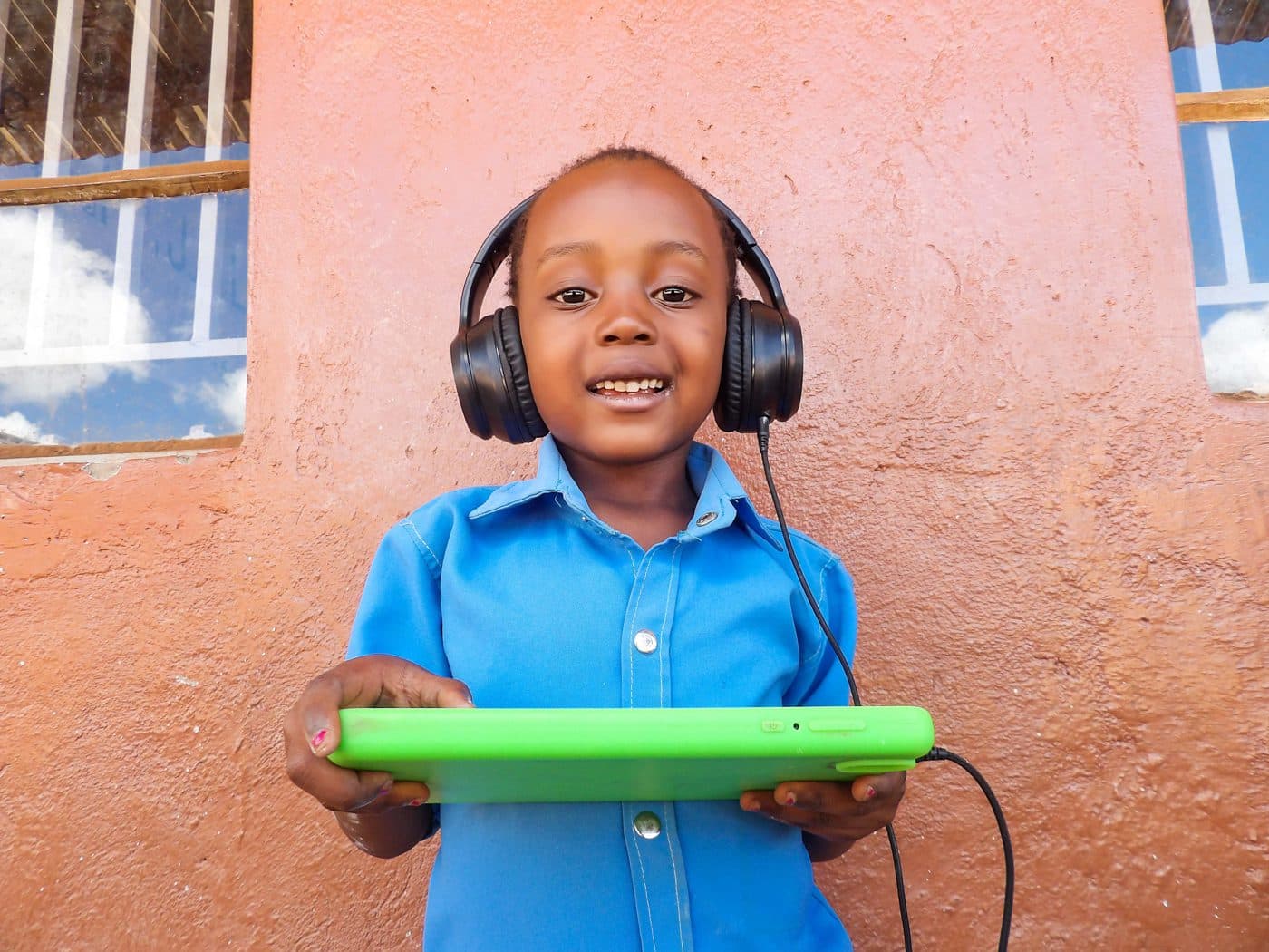 A young student at Dzaleka Refugee Camp smiling with headphones and a learning tablet